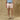 Person wearing light pink shorts and a blue shirt against a beige wall.